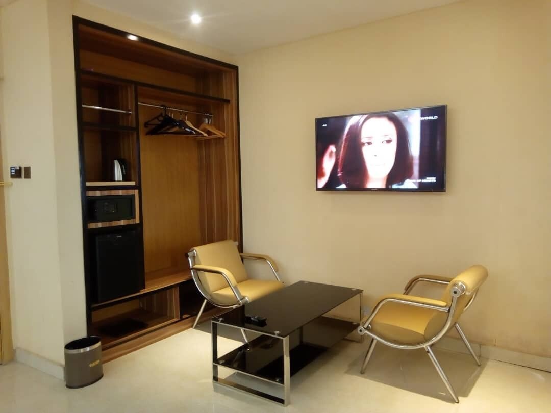A modern room with a wooden wardrobe, a television mounted on the wall, two chairs, and a small table.