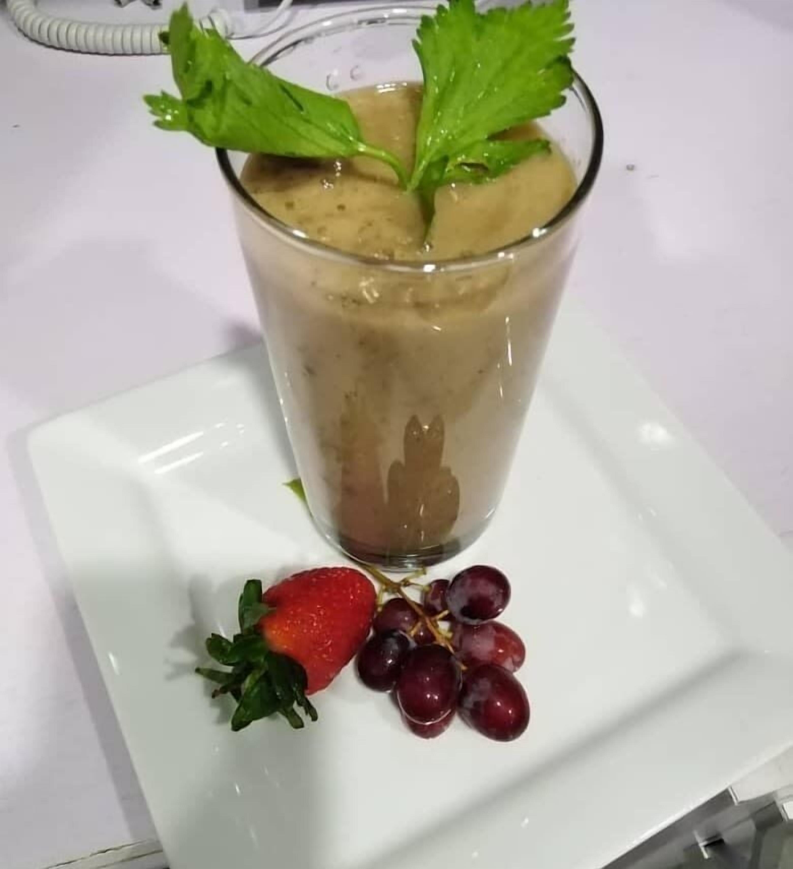 Un vaso de bebida helada con una fresa y uvas sobre un plato blanco.