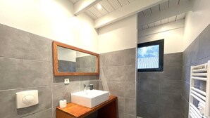 Ein modernes Badezimmer mit einem Holzbadschrank, einem weißen Waschbecken, einem Spiegel und einer Duschkabine.
