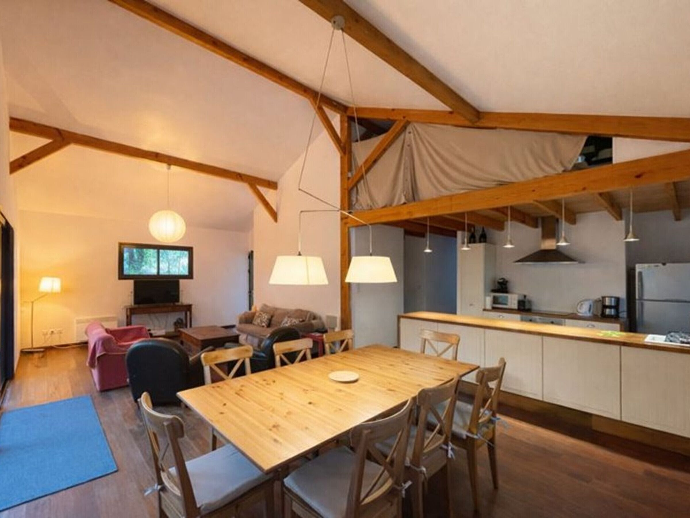 A cozy, open-plan living space with a wooden dining table, chairs, and a kitchen area.