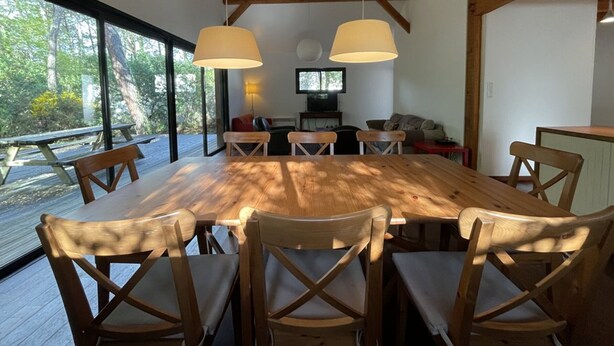 Un vaste espace dédié à la salle à manger, avec une grande table et des chaises en bois, deux lampes suspendues et une vue sur l’extérieur.