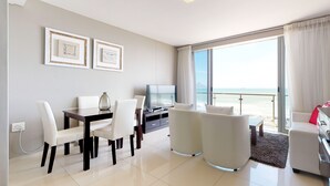 Une chambre d’hôtel moderne dotée d’un coin repas, d’une télévision et d’un balcon offrant une vue sur la plage.