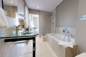 Un baño moderno con un lavabo de vidrio, una ducha a pie y una bañera grande.