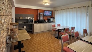 A compact kitchen with a microwave, coffee maker, and a TV on the wall. There is a dining area with a table and chairs. - Hôtel Charles (Les Arcs-sur-Argens)