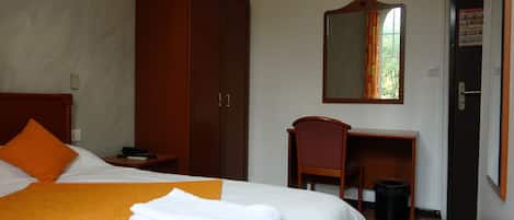 Una habitación de hotel con cama, escritorio, armario y espejo.
