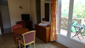 A room with a dining table, chairs, a TV, a cabinet, and a window with curtains. - Hôtel Charles (Les Arcs-sur-Argens)