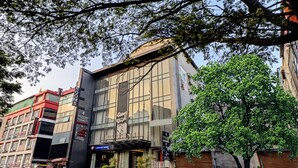Un edificio moderno con fachada de vidrio, un letrero que dice 'Paul's Inn Business Hotel' y un árbol en primer plano.
