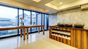 Habitación de hotel moderna con un ventanal grande, una mesa de madera, una zona de café y vistas a edificios.