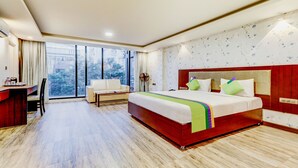 Habitación de hotel con una cama grande, un escritorio, una silla y vistas al exterior a través de un ventanal.