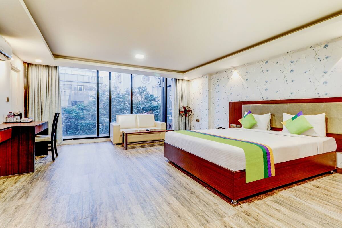 Ein Hotelzimmer mit einem großen Bett, einem Schreibtisch, einem Stuhl und Blick ins Freie durch ein großes Fenster.