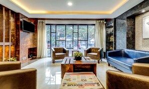 A modern living room with leather sofas, a coffee table, and a fireplace. Large windows offer a view of the city. - Treebo Trend Paul'S Inn (Bengaluru)