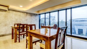 Un comedor con mesa y sillas de madera, ventanas amplias con vista a la ciudad e iluminación empotrada en el techo.