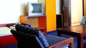 A room with a television on a shelf, a chair with a patterned cushion, and a wooden table.
