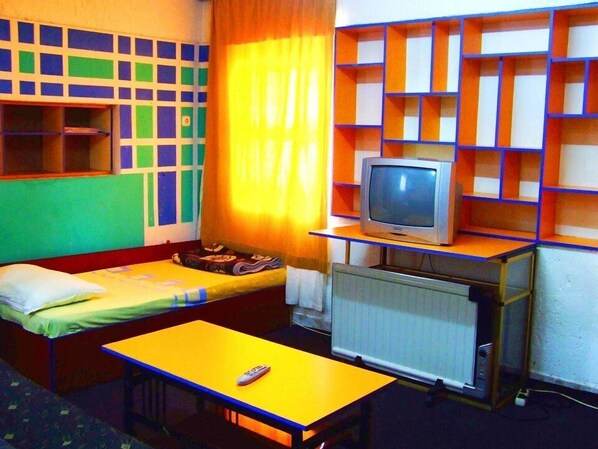 A room with a bed, a small table, a TV on a shelf, and a radiator.
