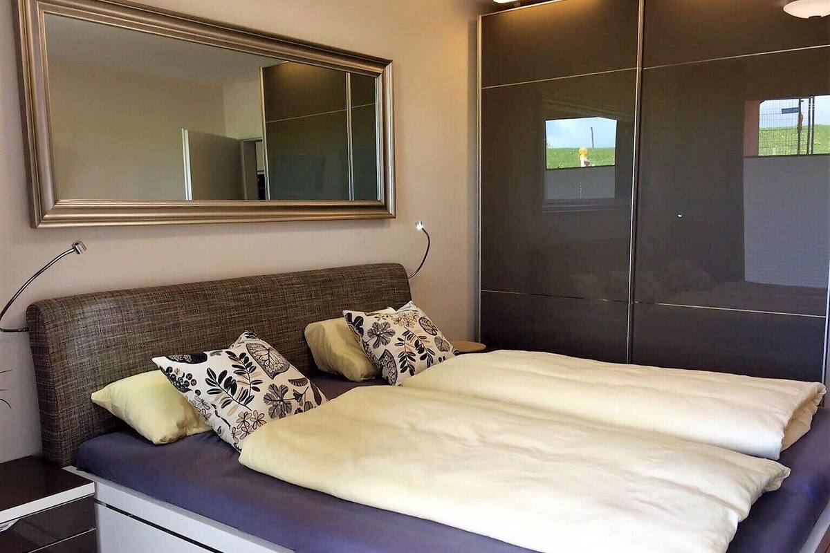 A bedroom with a large bed, a nightstand, a dresser, a mirror, and a wardrobe.