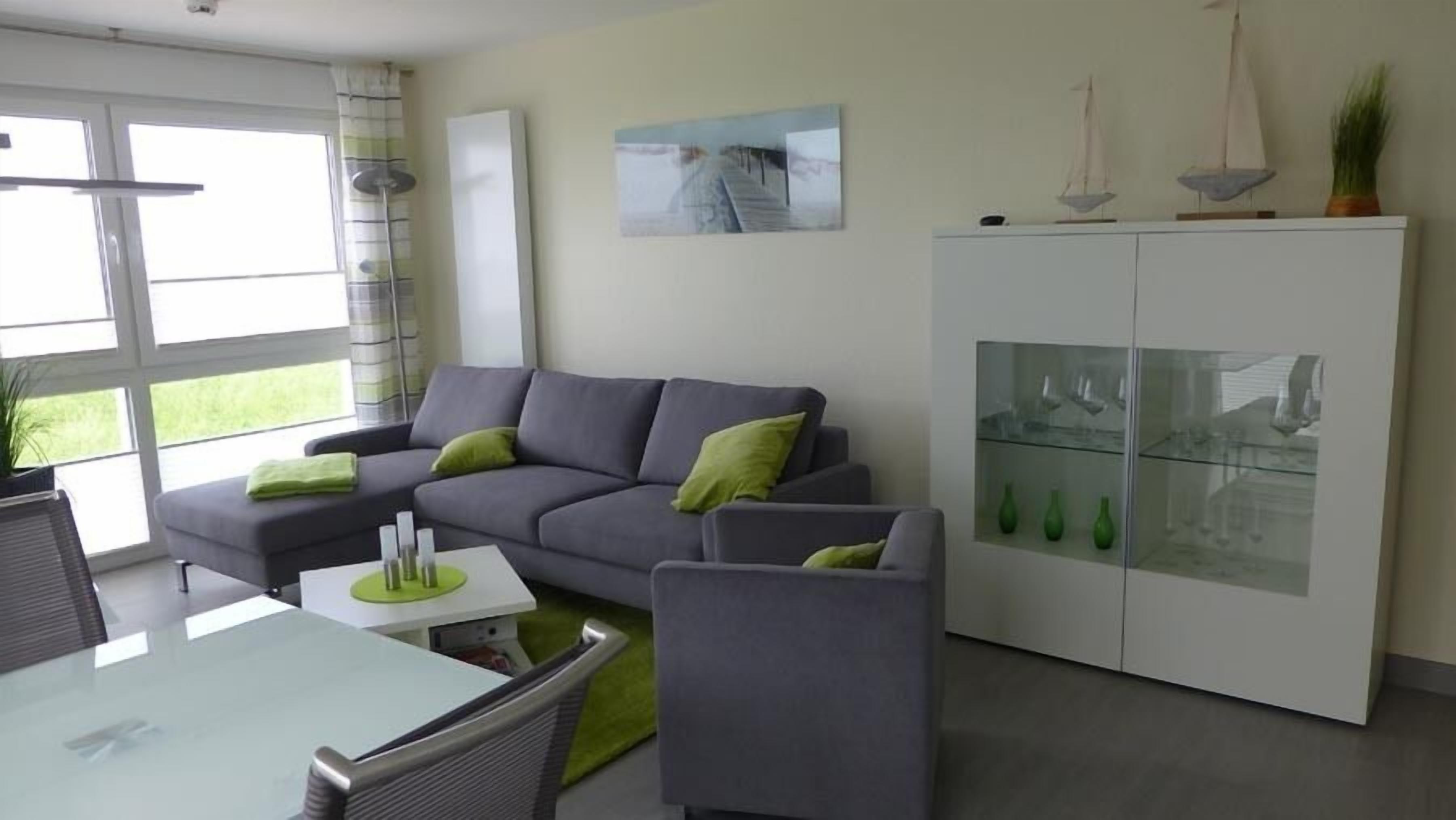 Een moderne woonkamer met een grijze bank, een eettafel en een kast met glazen deuren.