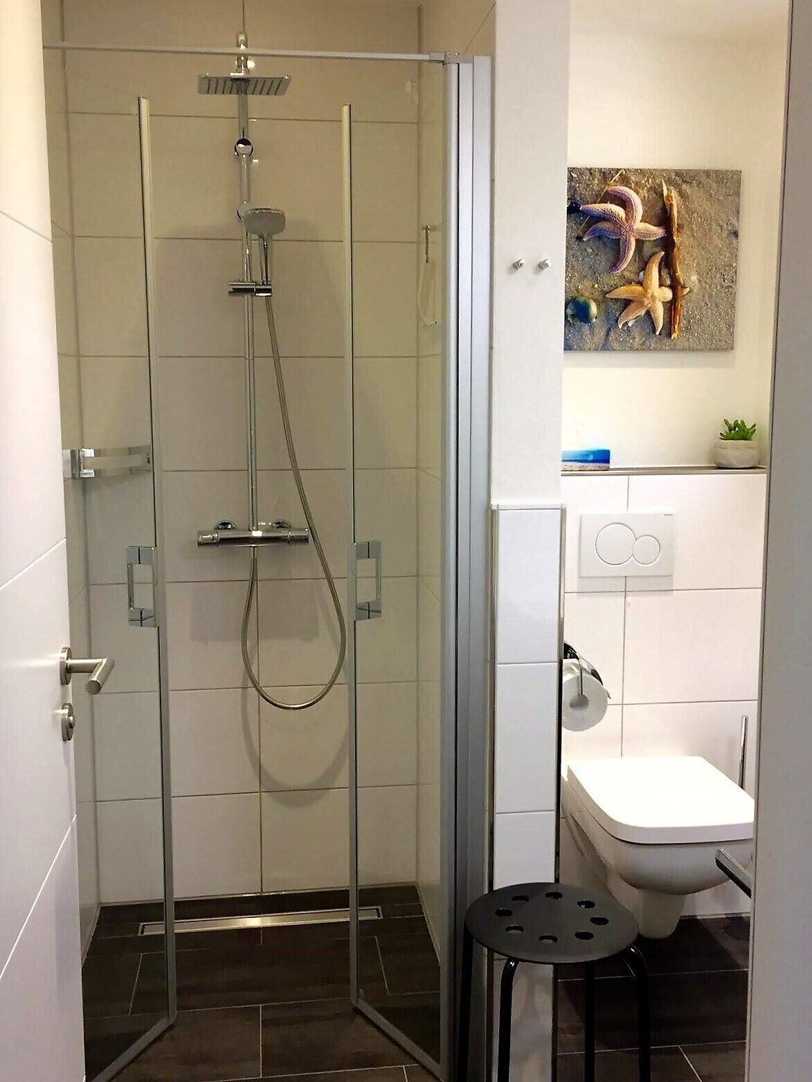 A modern bathroom with a glass-enclosed shower, a white toilet, and a small stool.