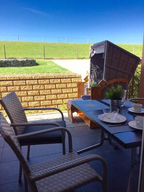 An outdoor patio with wicker chairs, a table set for dining, and a barbecue grill. - Residenz Windjammer (Cuxhaven)