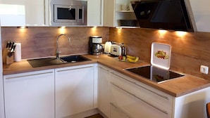 A modern kitchen with white cabinets, a stainless steel microwave, a sink, a toaster, and a small shelf with plants. - Residenz Windjammer (Cuxhaven)