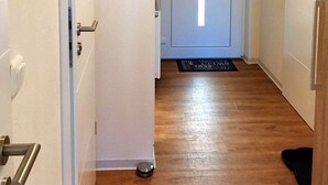 A hallway with a wooden floor, a white door at the end, and a black mat at the entrance. - Residenz Windjammer (Cuxhaven)