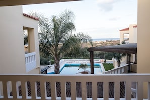 A pool area with a view of the sea, surrounded by palm trees and a white fence.
