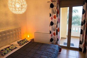 A bedroom with a bed, a radiator, a nightstand with a lamp, and a view of the outside balcony.