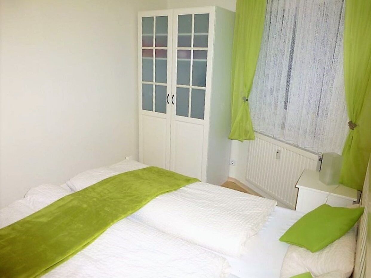 A bedroom with a bed, a wardrobe, a window with curtains, and a radiator.