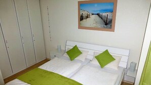 A bedroom with a bed, green pillows, a white headboard, a nightstand, a wall-mounted painting, and a wardrobe. - Haus Seemöwe (Cuxhaven)