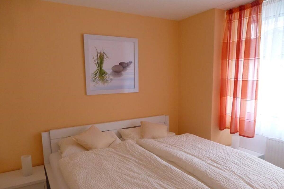 A bedroom with a bed, a nightstand, a framed picture on the wall, and a window with curtains.