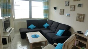 A compact living space with a sofa, a small table, a chair, a television, and a bookshelf. - Haus Seemöwe (Cuxhaven)