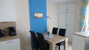 A small, modern kitchen with a coffee maker, a dining table with four chairs, and a blue accent wall. - Haus Seemöwe (Cuxhaven)