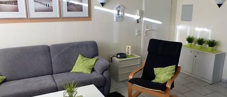 A living room with a grey sofa, a wooden chair, a white coffee table with a plant, and a cabinet with potted plants.