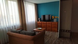 A living room with a wicker sofa, a wooden coffee table, a TV on a cabinet, and a door to the right. - Atelier Guesthouse (Filderstadt)