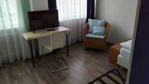 A room with a television on a small table, a wicker chair with a striped cushion, and a bed with white bedding. - Atelier Guesthouse (Filderstadt)