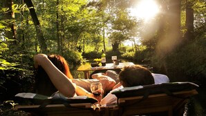 Two people reclining on wooden chairs outdoors, with a table between them holding a bottle of wine and a glass. - Spreewald Pension Spreeaue (Burg (Spreewald))