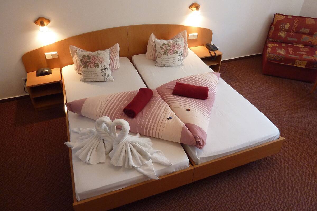 Ein Doppelbett mit zwei Kissen, ein Nachttisch mit Lampe und ein roter Sessel.