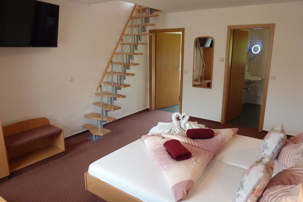 Ein Hotelzimmer mit Bett, Treppe, Fernseher und einem durchgehenden Türspalte sichtbaren Badezimmer.