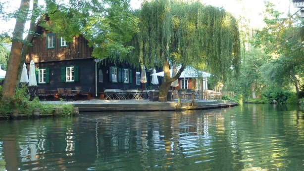A riverside building with outdoor seating and a dock. - Spreewald Pension Spreeaue (Burg (Spreewald))