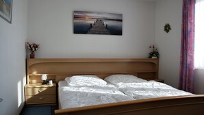 Ein ordentlich bezogenes Bett mit weißen Bettwäsche, ein hölzernes Kopfteil, ein Nachttisch mit Lampe und ein gerahmtes Bild von einem Steg an der Wand.