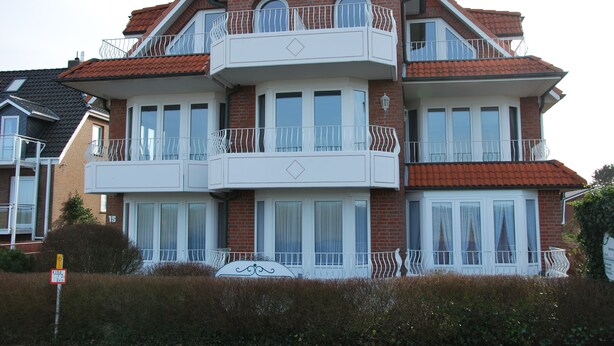 Ein mehrgeschossiges Wohngebäude mit Ziegel Fassade, weißen Balkonen und großen Fenstern.