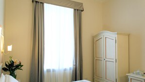 Ein Hotelzimmer mit einem Bett, einem Kleiderschrank, einem Nachttisch mit Lampe und einem Fenster mit Vorhängen.
