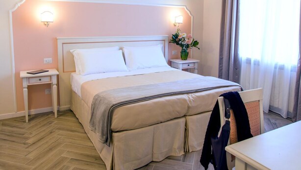 Ein Hotelzimmer mit Bett, Nachttischen, einem Sessel und einem Fenster mit Vorhängen.