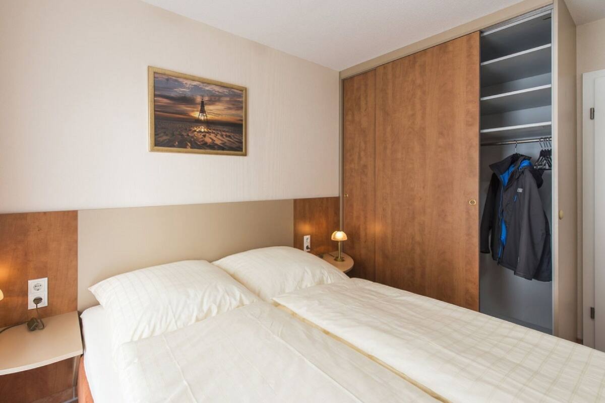 A hotel room with a bed, a nightstand, a lamp, a wardrobe, and a painting on the wall.