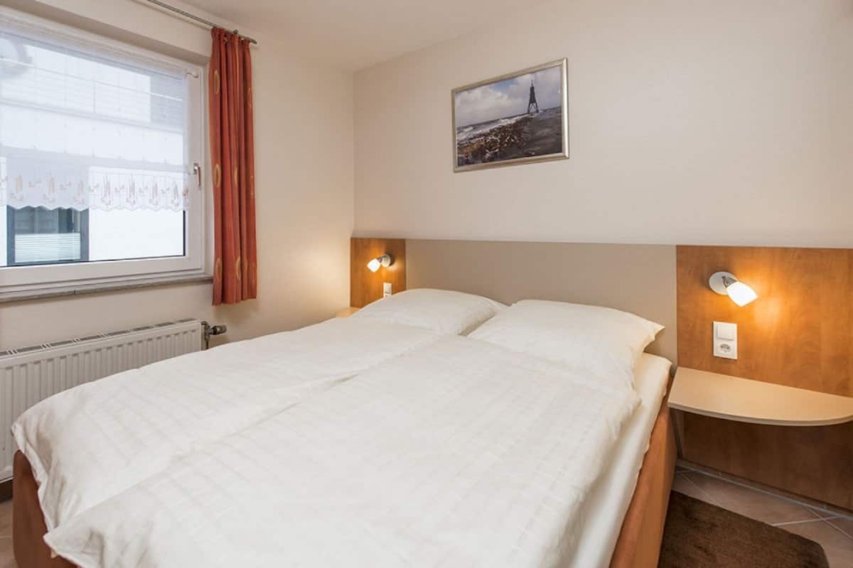 A hotel room with a large bed, two bedside tables with lamps, a window with curtains, and a picture on the wall.