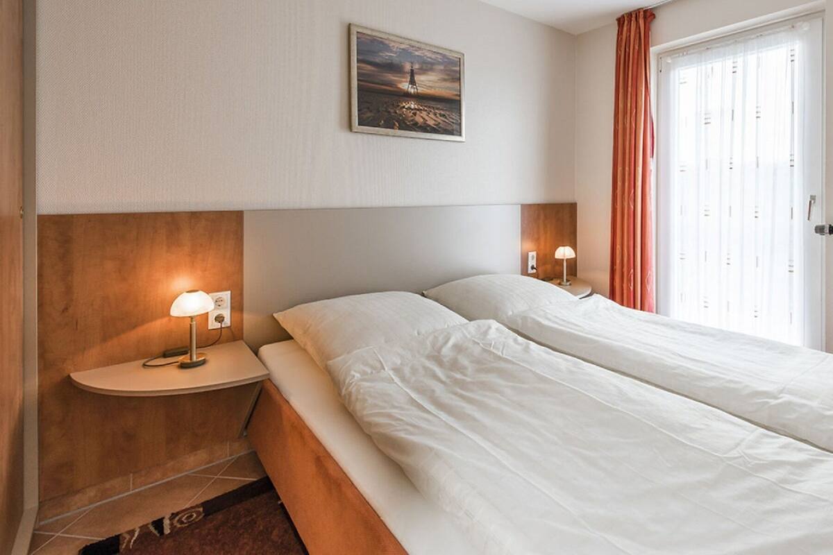 A hotel room with a double bed, two bedside tables with lamps, a painting on the wall, and a window with curtains.