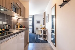 Une cuisine moderne équipée d’un lave-vaisselle, d’un four à micro-ondes et d’une bouilloire, qui donne sur un coin repas avec une table et des chaises.
