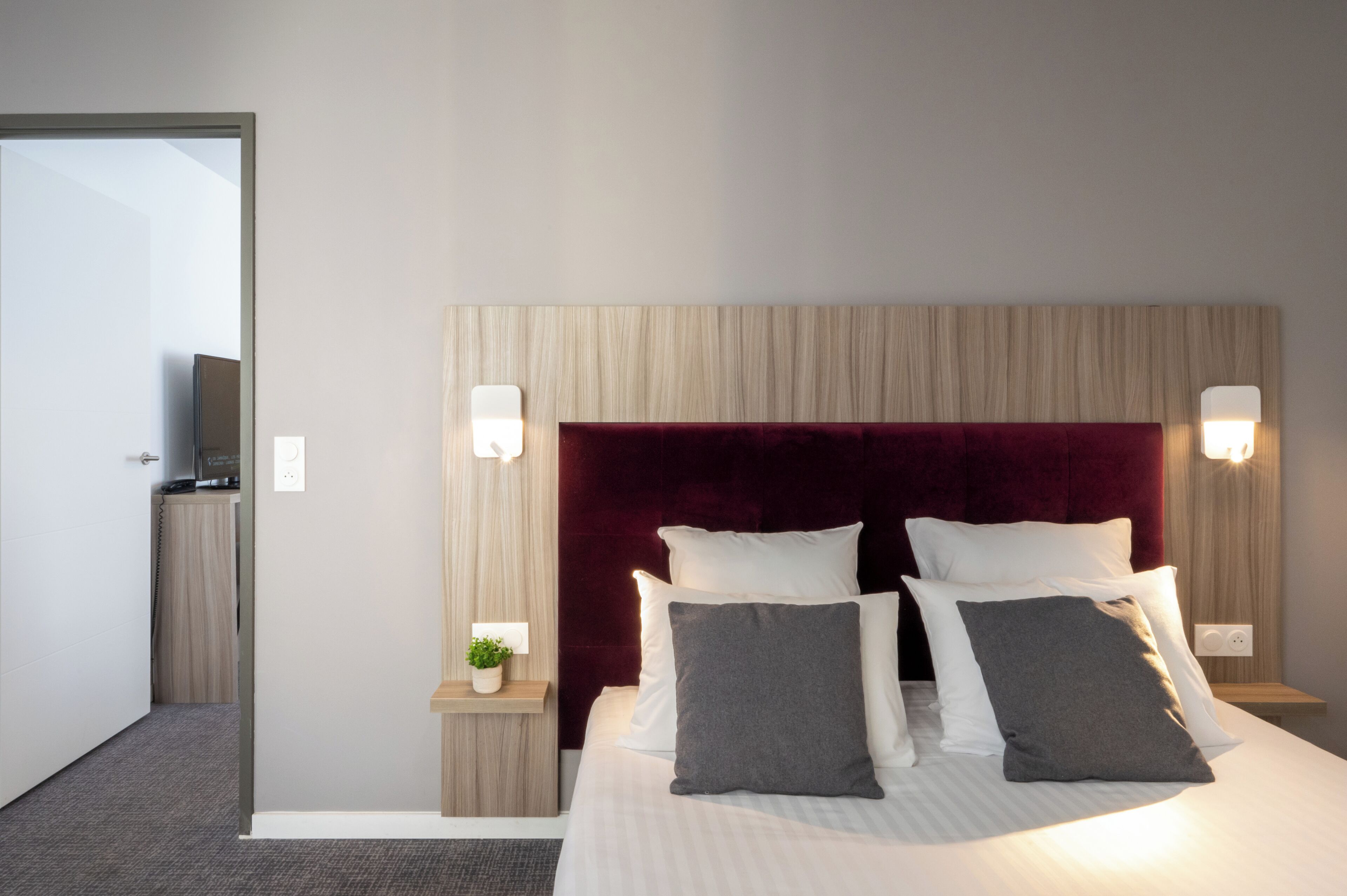 Quarto de hotel com uma cama grande, duas mesinhas de cabeceira, uma televisão e um painel de madeira na cabeceira.