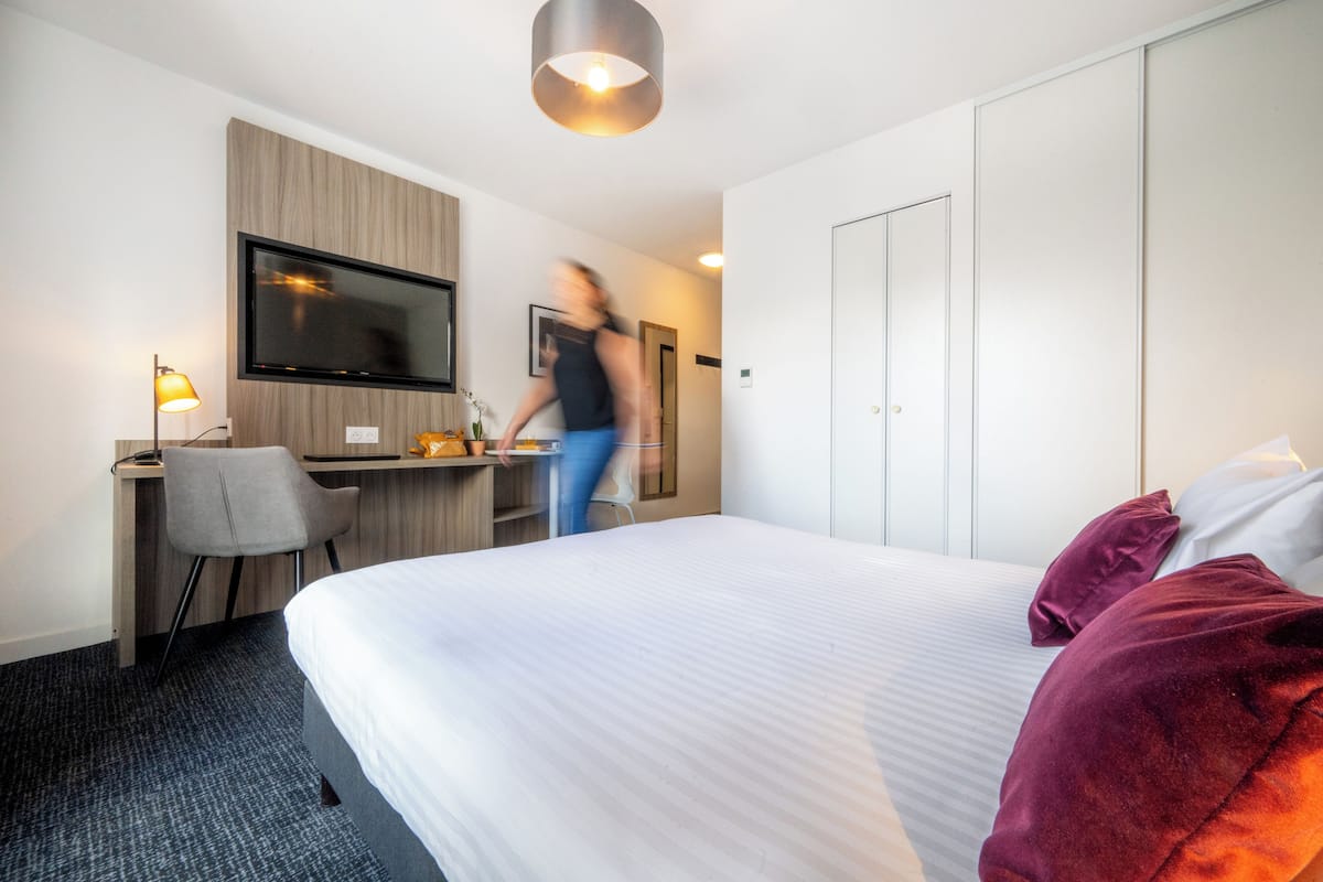 Ein modernes Hotelzimmer mit einem großen Bett, einem Schreibtisch mit Stuhl, einem Fernseher und einem Kleiderschrank.