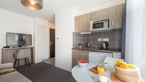 Moderni keittiö, jossa on mikroaaltouuni, leivänpaahdin ja kahvinkeitin. Keittiössä on ruokapöytä, jonka päällä on aamiaisruokia ja erillinen kori täynnä hedelmiä.