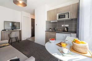 A modern kitchen with a microwave, a sink, and a dining area with a table set for breakfast. - Nemea Appart Hotel Grand Cœur Nancy Centre (Nancy)
